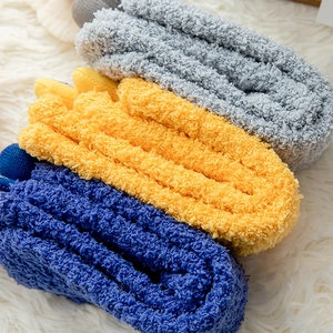 Close-up of thick coral fleece socks in grey, yellow and navy blue on plush white rug