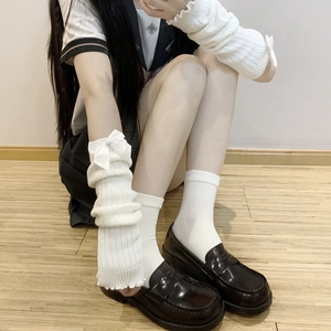 Close-up of white knitted leg warmers featuring satin ribbons and ribbed texture detail