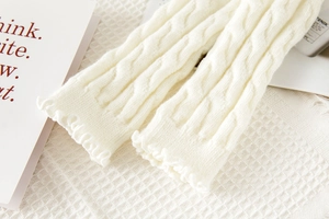 Detailed knit texture of ivory leg warmers featuring classic cable stitch and ruffle edges