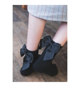 Dettaglio ravvicinato di calze nere stile Lolita con fiocco su pavimento in legno vintage