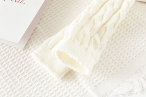 Detailed macro view of white cable knit leg warmers showing thick ribbed wool texture