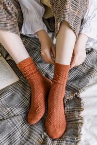 Detailed close-up of orange wool blend knit socks with vintage diamond and cable patterns