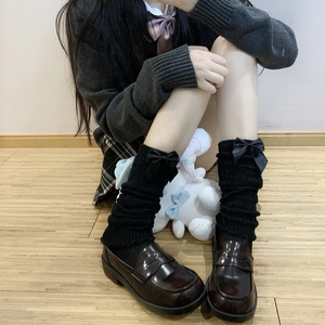 Close-up of black knitted JK leg warmers with satin bows and brown platform loafers