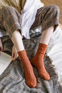 Close-up of caramel orange winter wool socks with retro diamond knit texture on a rug