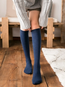 Detail of dark blue knee-high socks with ribbed elastic cuffs on model in cozy home setting