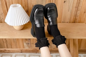 Detail of black frilly Lolita socks paired with vintage matte loafers on a bench