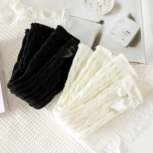 Close-up of cable knit leg warmers with ribbon bows on a waffle texture background