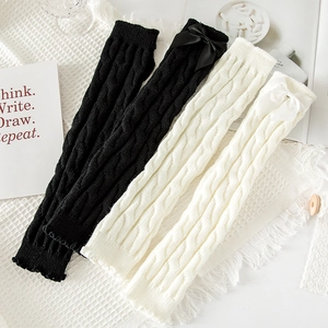 Close-up of cable-knit leg warmers with satin bow detail and thick wool texture