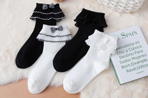 Detail of white and black Lolita socks with layered lace ruffles and plaid bows on plush rug