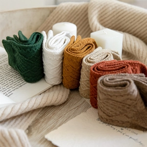 Close-up of cable knit textures on various colored winter wool socks in a wooden tray