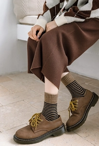 Détail de chaussettes rayées bouclées avec chaussures en cuir marron et jupe plissée