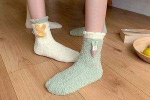 Detail of coral fleece socks with cute rabbit and carrot plush patches on wooden floor