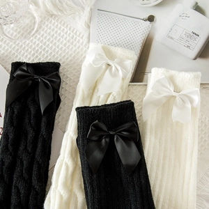 Close-up of cable-knit leg warmers with large satin bows in black and beige colors