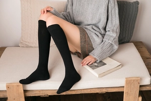 Close-up of black knee-high socks in cotton knit on a model wearing a plaid skirt