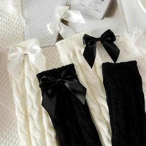 Detailed close-up of chunky knit leg warmers featuring elegant satin ribbon bows