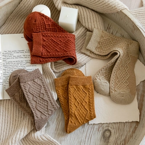 Close-up of vintage knit socks in warm autumn tones on a wooden tray with cozy props