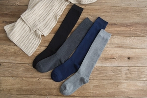 Flat lay of four-color knit cotton knee-high socks in black, grey, and navy on wood