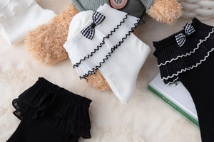 Detail of white and black JK style socks with lace ruffles and plaid bow accents
