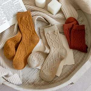 Detailed knit texture of ginger and brick red wool socks in a cozy wooden tray setting