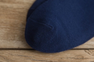 Close-up of navy blue knit socks featuring premium seamless toe stitching on wood background