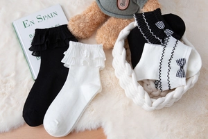 Detail of white Lolita socks with ruffled lace edges and black bows on soft plush rug