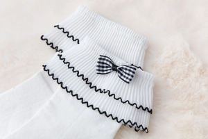 Detail of white ribbed cotton socks featuring black scalloped trim and plaid bow detail
