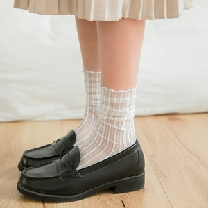 Detail view of white lace ruffle socks paired with black leather loafers on wood floor