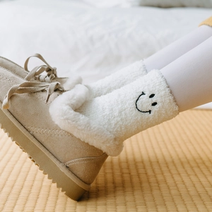 Detail of warm beige suede boots and white coral fleece socks with embroidered smiley face