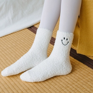 Detail of white coral fleece socks featuring black smiley embroidery on soft texture