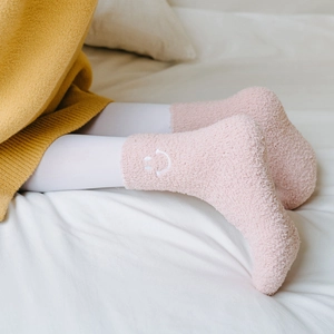 Close-up of pink coral fleece socks featuring cute white smiley face embroidery