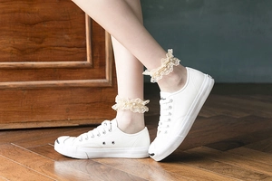 Détail de chaussettes en dentelle à perles portées avec chaussures en toile blanches