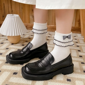 JK style white crew socks with black ruffled edges and bow paired with black platform loafers