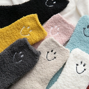 Close-up of thick coral fleece socks featuring embroidered smiley faces in multiple colors