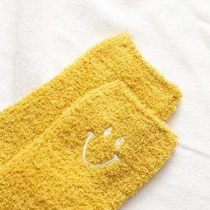 Detailed close-up of warm yellow coral fleece socks with embroidered smiley face design