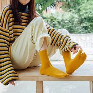 Detail of ginger yellow split-toe socks with vertical ribbed knit texture worn with a sweater