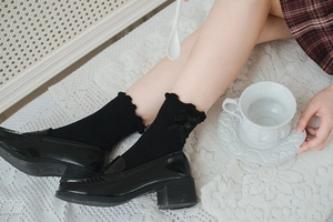 Detail of black mid-calf socks with ruffle trim and bow accents worn with loafers
