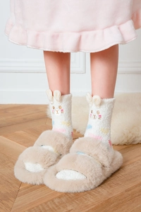 Close-up of fluffy white bunny ear coral fleece socks and plush beige slippers on a rug