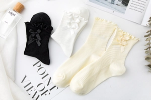 Close-up of knit crew socks with lettuce edge trim and ribbon bows in black and white
