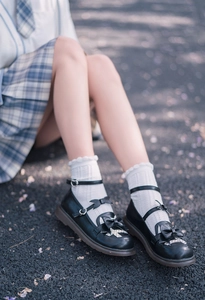 Detail of white lace frill socks paired with black Mary Jane shoes and a plaid JK skirt