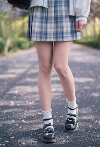 Close-up of Mary Jane shoes with bows and white ruffle socks on a flower-strewn path