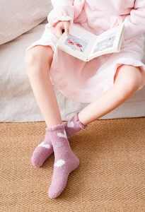 Detail of plush winter coral fleece socks with white heart patterns in a cozy home setting