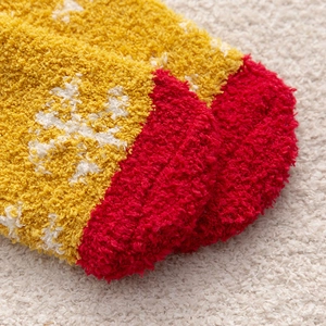 Close-up of fluffy yellow and red coral fleece Christmas socks with white snowflake patterns