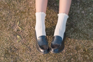 Close-up of white lace frill knit socks with black loafers on grass for a retro style