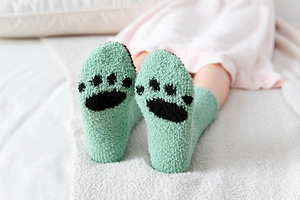 Detail von weichen grünen Korallenvlies-Socken mit Katzenpfoten-Print auf Teppich