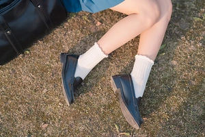 Detail of white cotton crew socks with ruffle trim paired with black loafers