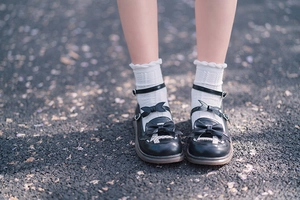 Detail of black Lolita shoes with double bows, heart buckles and white lace frill socks