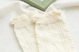 Dettaglio ravvicinato di calze in maglia crema con motivi a cuore e bordi a balze