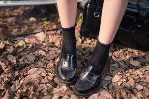 Detail of black leather loafers paired with frilly crew socks on autumn leaves