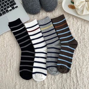 Detailed view of four pairs of striped mid-calf socks displayed on a white plush carpet