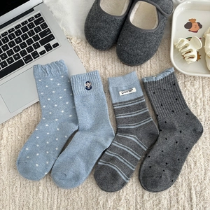 Detail view of four pairs of thick wool socks in blue and gray patterns on a soft mat